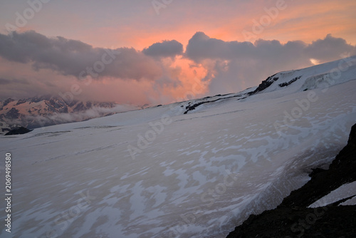 Snow-covered slope in the Mount Elbrus region during sunset, illuminated by warm evening colors across the sky.