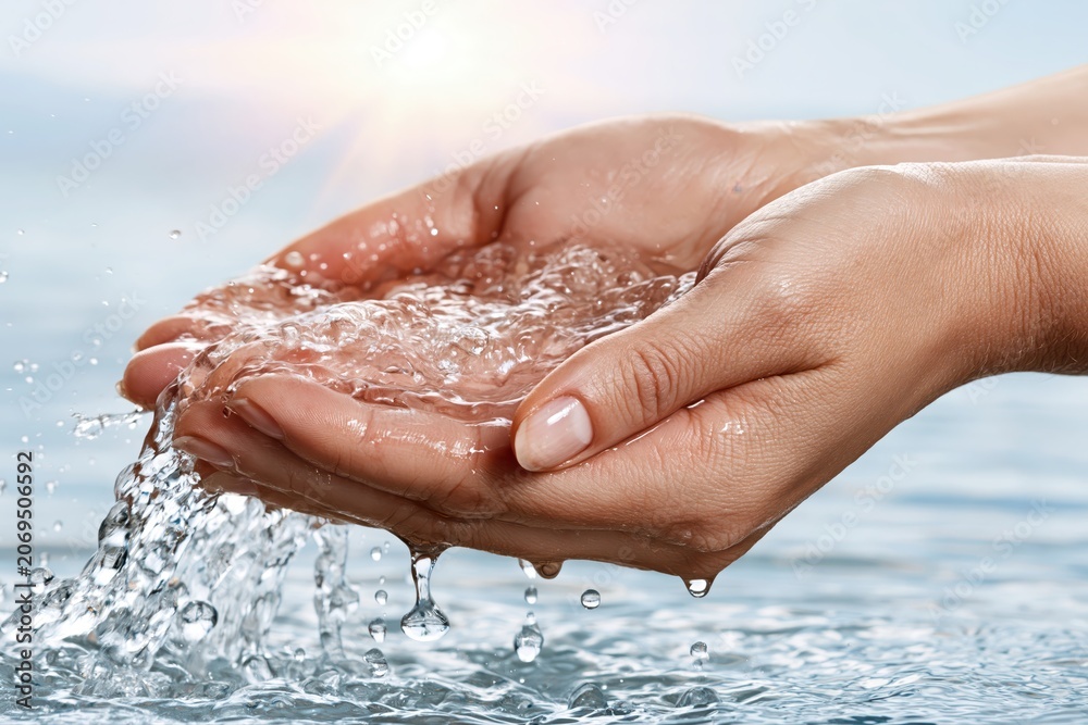 Fototapeta premium Close-up of cupped hands holding clear flowing water with sunlight shimmering on the surface.