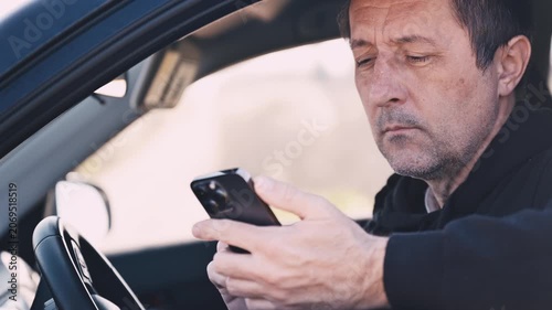 Mature man sitting in car checking smartphone while waiting, everyday commute and mobile use concept, 4K