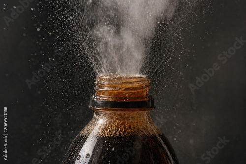 Open plastic soda bottle spraying foam and droplets.