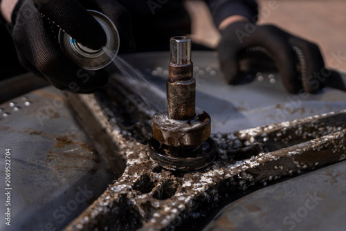 Photography Technician hand spraying penetrating lubricant lubricant onto a rusty spider arm bracket shaft of a disassembled stainless steel washing machine drum during appliance repair service