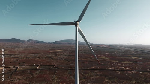 Drone flight around a wind turbine above volcanic terrain in Fuerteventura, Canary Islands, Spain. Renewable energy infrastructure surrounded by arid landscape and mountains.