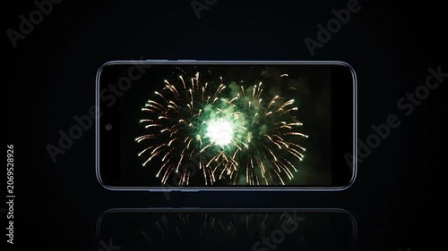 A smartphone displays bright green fireworks on a dark screen
