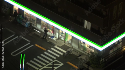 TOKYO, JAPAN - JUNE 2026 : Aerial view of convenience store at night. Glowing neon lighted konbini shop entrance on urban street. Japanese nightlife and urban lifestyle concept video.
