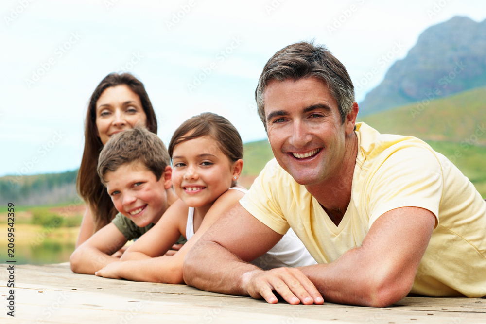 Fototapeta premium Portrait, happiness and family in nature for travel, together or bonding with summer vacation. People, parents and kids with smile outdoor, holiday break and relax on pier for connection and getaway