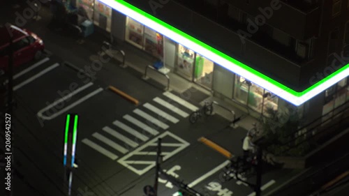 TOKYO, JAPAN - JUNE 2026 : Aerial view of convenience store at night. Glowing neon lighted konbini shop entrance on urban street. Japanese nightlife and urban lifestyle concept video. Time lapse shot.