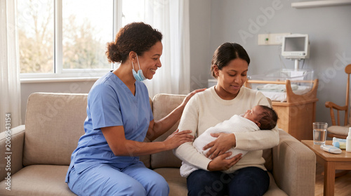 Female nurse in blue scrubs comforting a new mother who is holding her sleeping newborn on a sofa in a maternity room setting, ideal for postpartum care and maternity healthcare content.