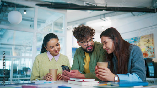College friends gathering at desk with coffee cups. Group students watching funny video on smartphone. Male holding mobile device and sharing content. Classmates relaxing together in campus study area