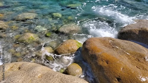 Clear ocean waves crash against smooth coastal rocks