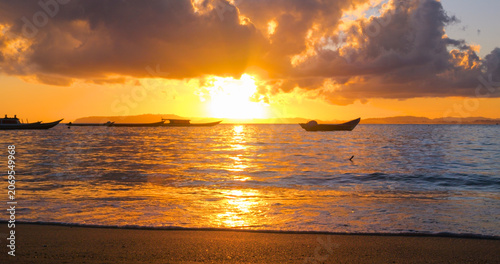 Fotografía SILHOUETTE, LENS FLARE: Boats rest on calm sea under dramatic sunset sky