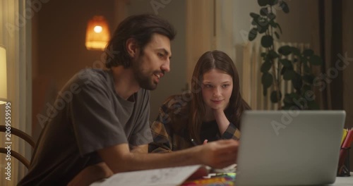 Man and teenage girl talking beside a laptop in a cozy home interior