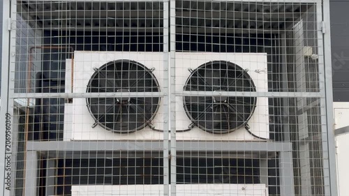 Industrial HVAC cooling fans mounted on retail store exterior behind protective metal grille. Concept: commercial ventilation, air conditioning and equipment maintenance.