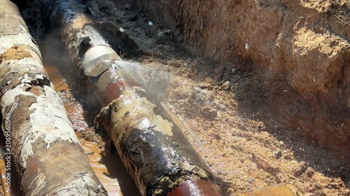 Pipeline accident: hot water jets gushing from a rusted pipe in a dug trench