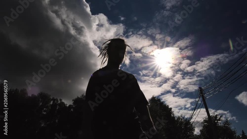 A silhouette of a man with long dreadlocks playing basketball against the backdrop of the sky and bright sun