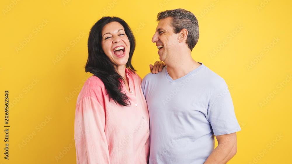Naklejka premium Cheerful adult man and woman sharing a moment of genuine laughter and joy, embracing partnership and togetherness on yellow background