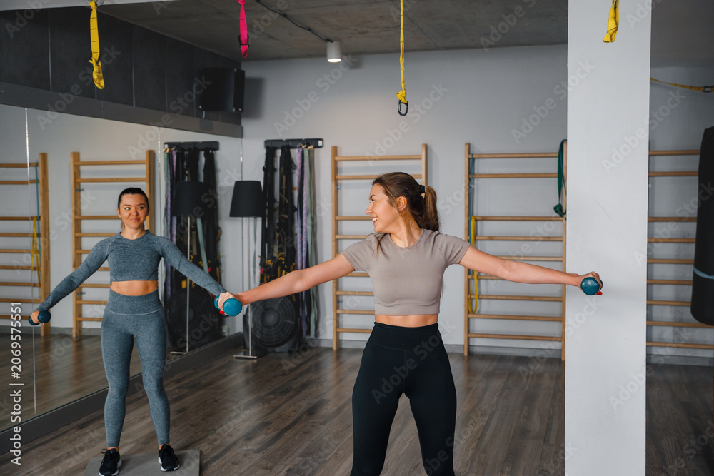 Fototapeta premium Two women work out with dumbbells in a gym during training session in a modern fitness studio