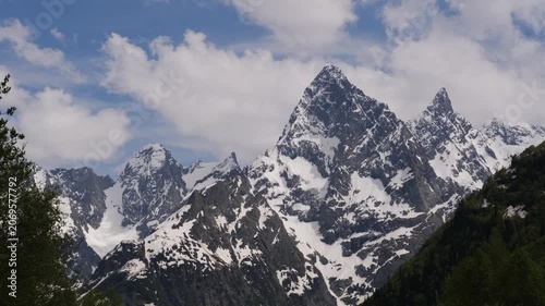 Snow-covered peaks tower against a bright blue sky filled with clouds, revealing the beauty of a mountainous landscape in springtime