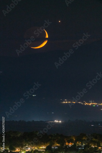 Spectacular orange crescent moon and bright star setting over mountain peaks