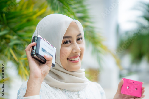 A young Asian Muslim woman is listening to music on a walkman and holding a cassette.