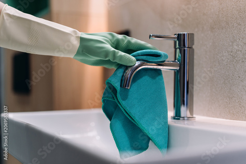 фотографія Woman cleans faucet and bathroom sink in modern apartment