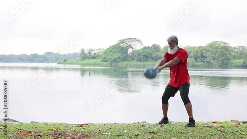 Mature Indian man with a beard working out with a kettlebell in a lakeside park In Singapore.