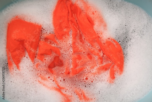 Bild auf Leinwand Orange garment in suds, top view. Hand washing laundry