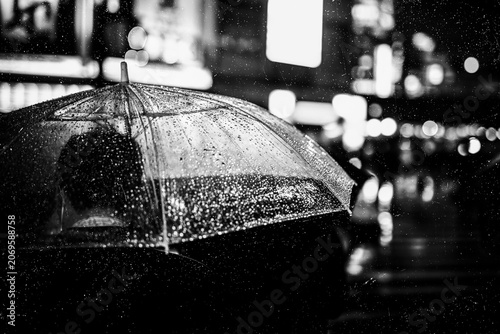 Fotografie Rainy night with umbrella in bustling city lights