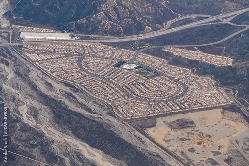 Aerial view of a residential subdivision surrounding Paakuma K-8 School in the Verdemont/Devore area of San Bernardino, with the San Bernardino Mountains foothills and I-15/I-215 interchange visible, 