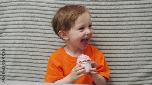 Child Eating, cupcake for dessert, sweet treat or sugar snack . Boy Bite, tasting vanilla cake with pink cream on top, hungry and enjoy delicious food. Happy childhood: a child enjoys a sweet treat