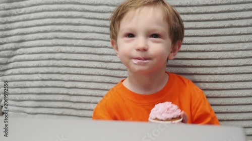 Child Eating, cupcake for dessert, sweet treat or sugar snack . Boy Bite, tasting vanilla cake with pink cream on top, hungry and enjoy delicious food. Happy childhood: a child enjoys a sweet treat