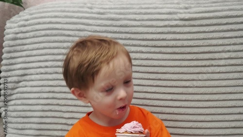 Child Eating, cupcake for dessert, sweet treat or sugar snack . Boy Bite, tasting vanilla cake with pink cream on top, hungry and enjoy delicious food. Happy childhood: a child enjoys a sweet treat