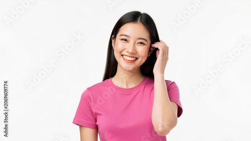 Smiling Asian Woman in Pink T-Shirt: A young Asian woman with long, dark hair smiles warmly and touches her hair.