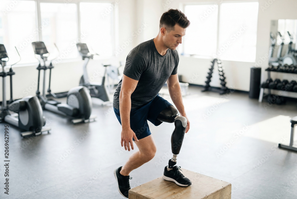 Fototapeta premium Man with prosthetic leg doing box jump exercise in modern gym