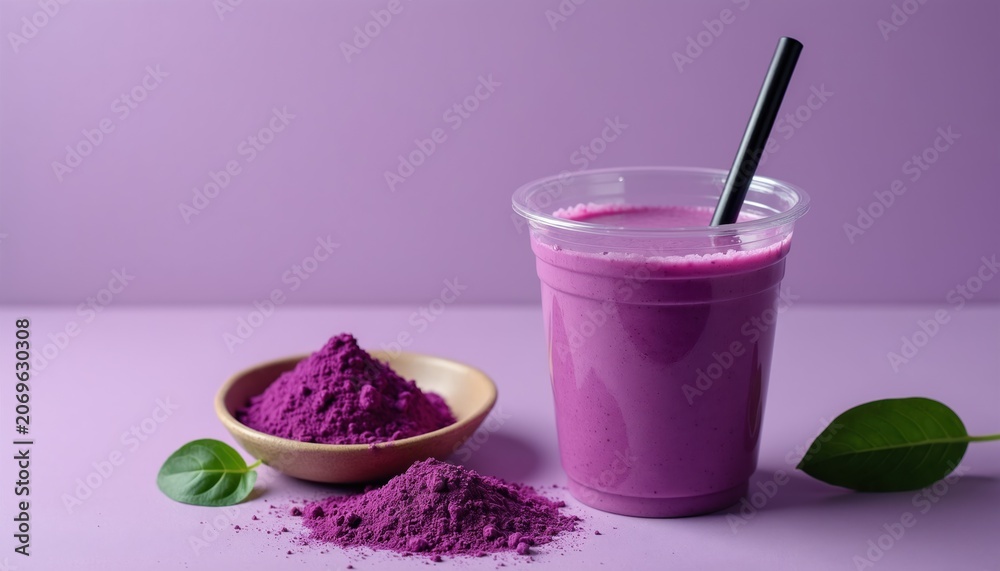 Fototapeta premium Purple ube smoothie in clear cup with straw. Ube powder in small bowl and on table. Green leaf nearby. Health drink, vibrant color, light purple background.