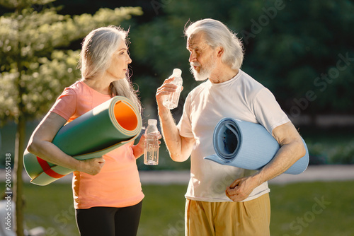 Senior couple with exercise mats standing at park and talking