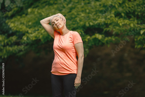Senior woman standing at summer park and doing excercises