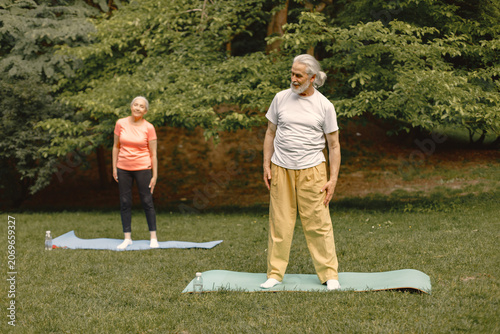 Senior couple standing at summer park and doing excercises on a yoga mats