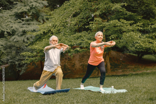 Senior couple standing at summer park and doing excercises on a yoga mats