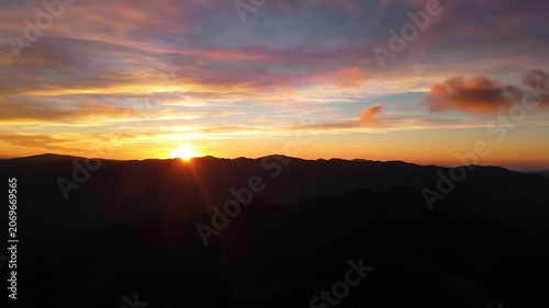 Golden sun rises over dark mountain silhouettes under orange clouds