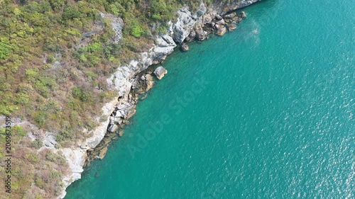 Vibrant turquoise ocean and rugged green cliffside backdrop showcase Containers highlighting global trade logistics amidst breathtaking coastal waterway beauty at this scenic location.