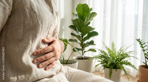 Woman holding her stomach in pain sitting at home with indoor plants