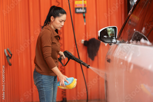Obraz na plátně woman washing a car with water hose and sponge in a self-service car wash statio