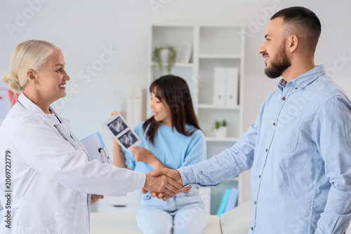 Female fertility doctor with couple shaking hands after IVF in clinic