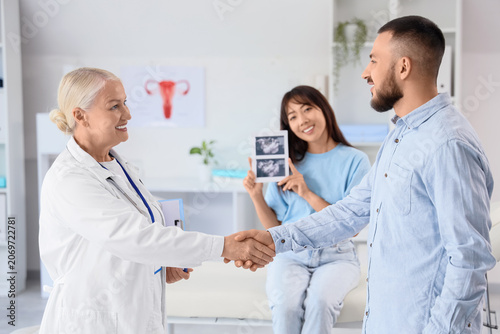 Female fertility doctor with couple shaking hands after IVF in clinic