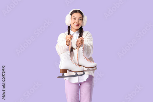 Happy young Asian woman with ice skates on lilac background