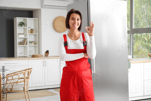 Female worker showing OK near fridge in kitchen