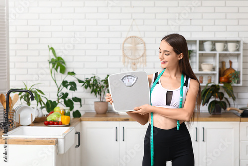 Sporty young woman with weight scales and tape measure in kitchen. Diet concept