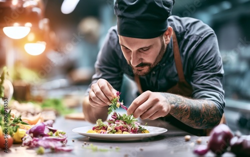 Expert chef meticulously plating gourmet dish with fresh ingredients in modern kitchen for culinary presentation