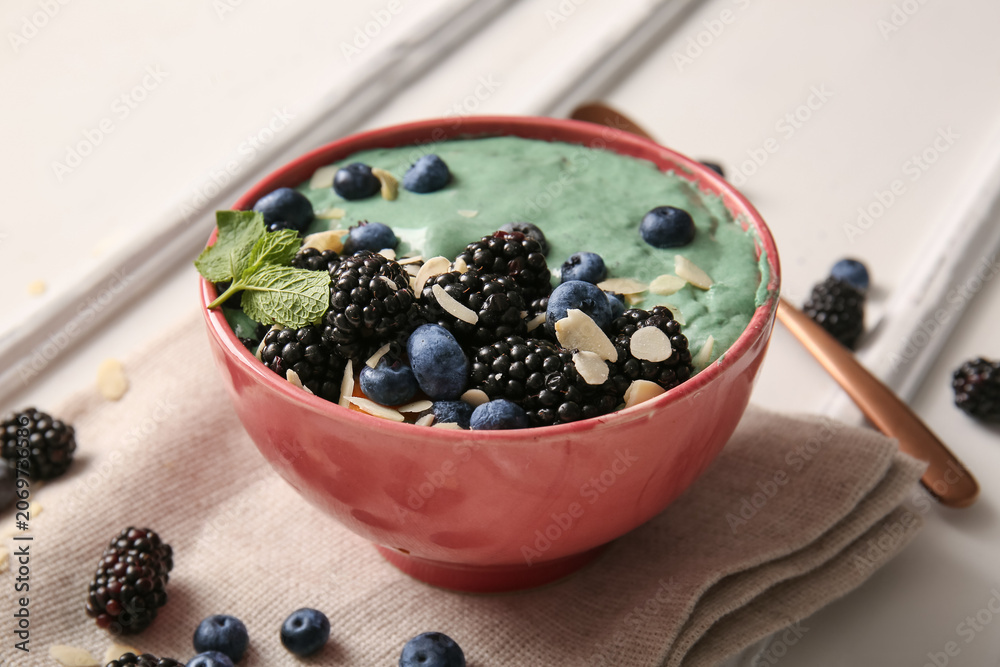 Naklejka premium Napkin, bowl with tasty spirulina smoothie and berries on white background, closeup