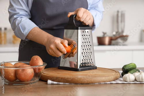 Woman grating carrot at tab...